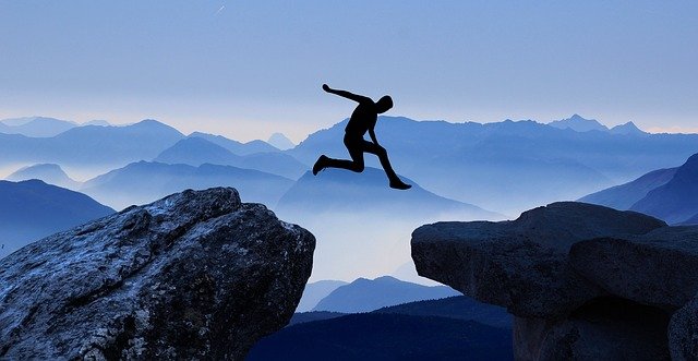 A person makes a great leap between two rocky outcrops, representing the large organisational changes business leaders must often tackle.