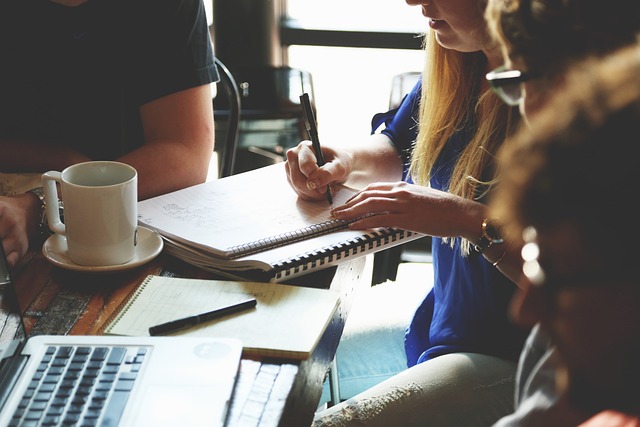 A business meeting. A woman is taking notes in a pad.